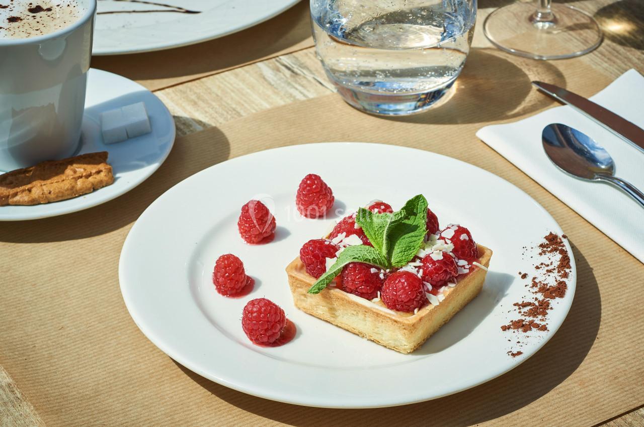 Tartelette garnie de framboises fraîches, décorée de menthe, servie sur une assiette blanche avec des couverts.