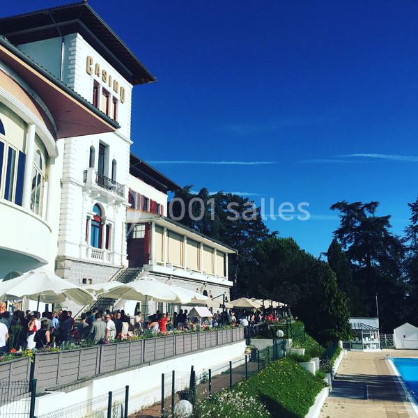 Façade d'un bâtiment avec l'inscription ’Casino’, terrasse animée, parasols blancs et piscine en contrebas.