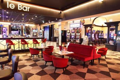 Salle de casino avec machines à sous illuminées, chaises noires et décor moderne sous un plafond sombre.