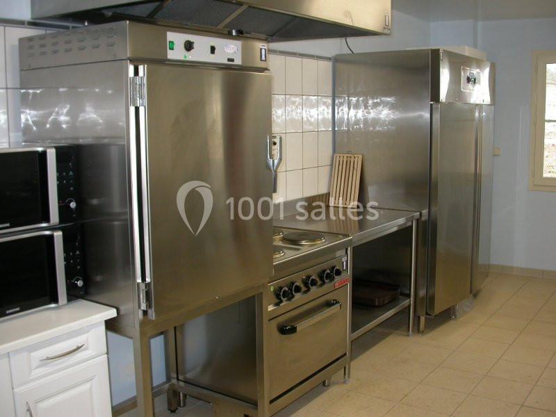 Cuisine professionnelle équipée d'appareils en inox, incluant four, plaques de cuisson, réfrigérateurs et micro-ondes.