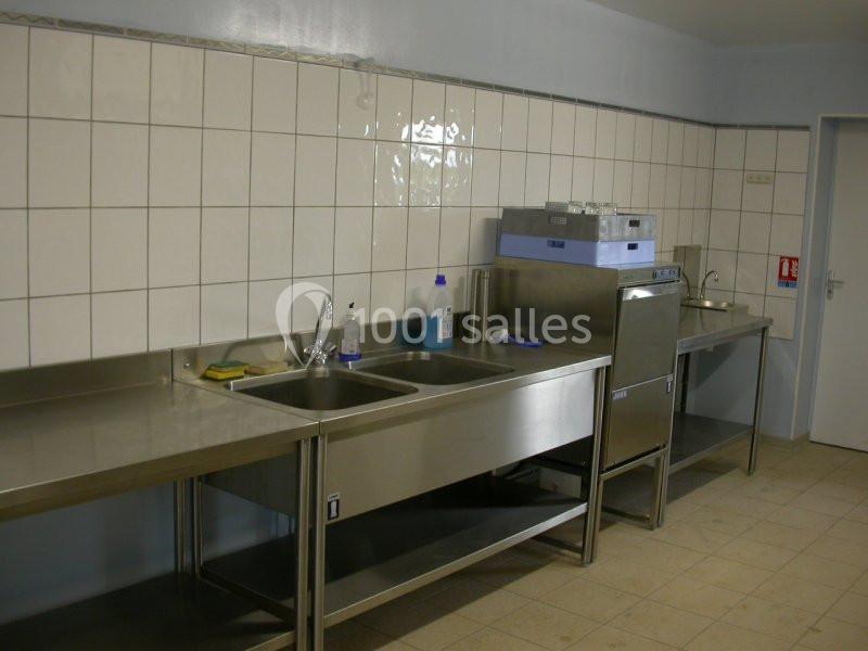 Cuisine professionnelle avec plans de travail en inox, évier double, lave-vaisselle industriel et carrelage mural blanc.