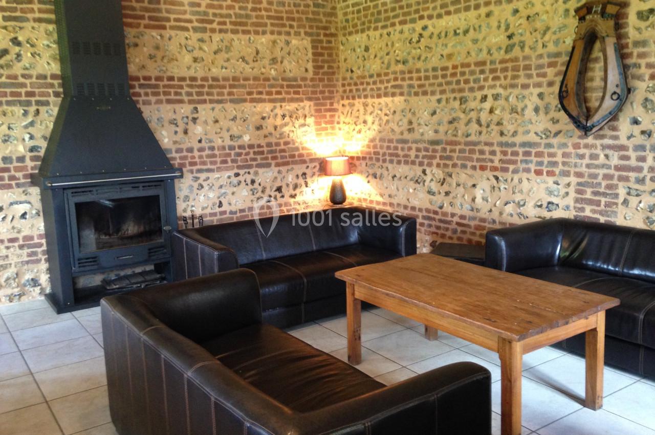 Salon avec murs en briques et pierres apparentes, cheminée noire, trois canapés en cuir et table basse en bois.