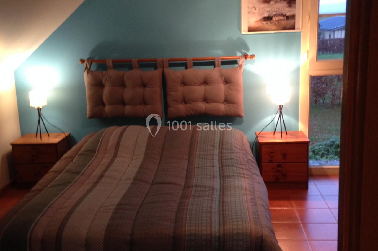 Chambre avec un lit double, mur bleu, deux tables de chevet en bois avec lampes et une fenêtre donnant sur un jardin.