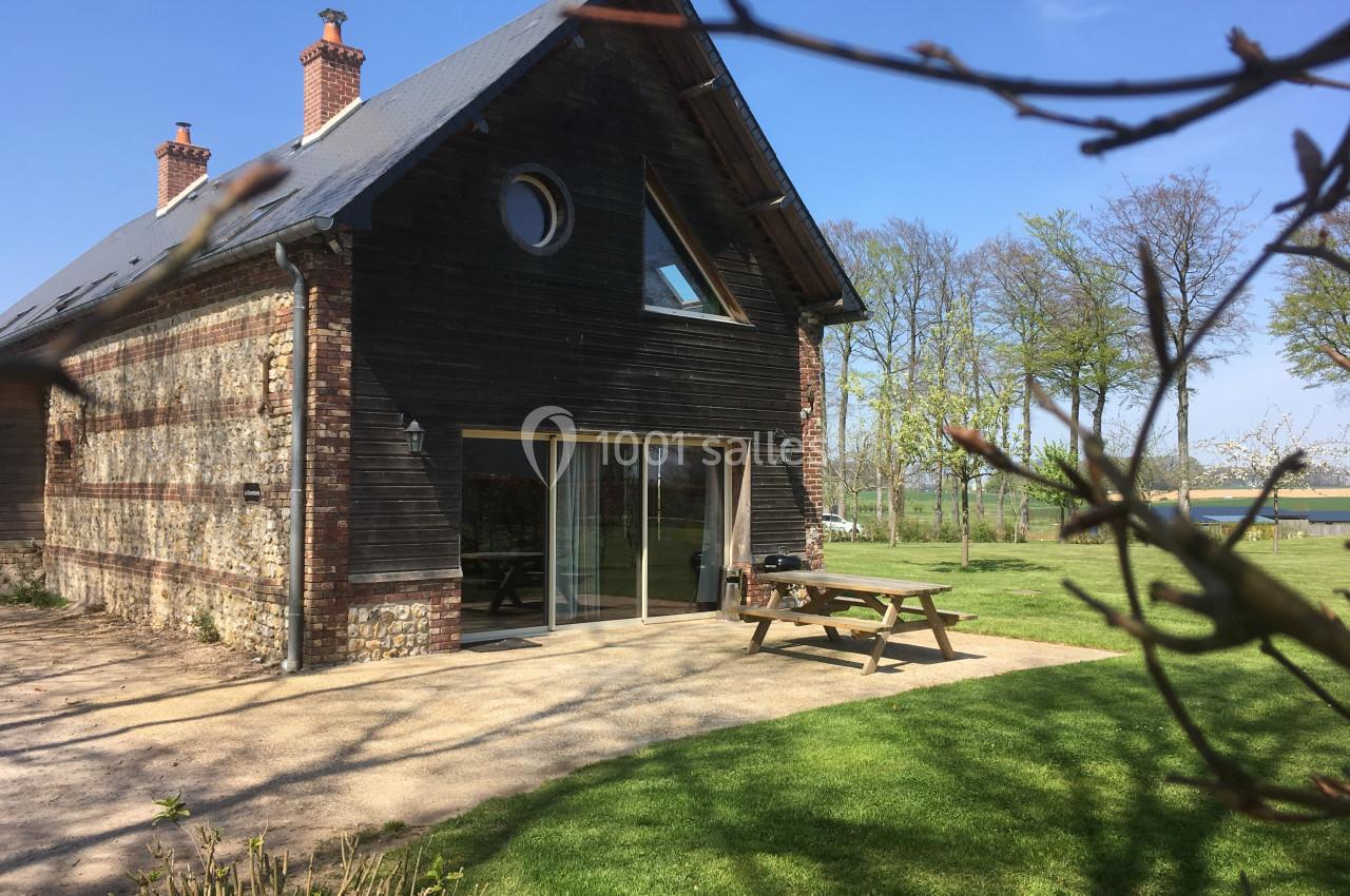 Maison en bois et briques avec terrasse, table de pique-nique et jardin verdoyant sous un ciel bleu.