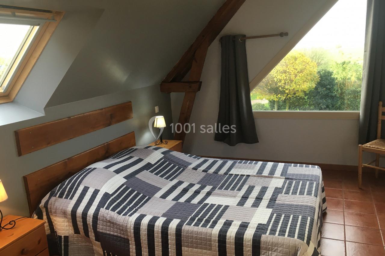 Chambre mansardée avec lit double, couvre-lit à motifs géométriques, poutres apparentes et vue sur jardin.