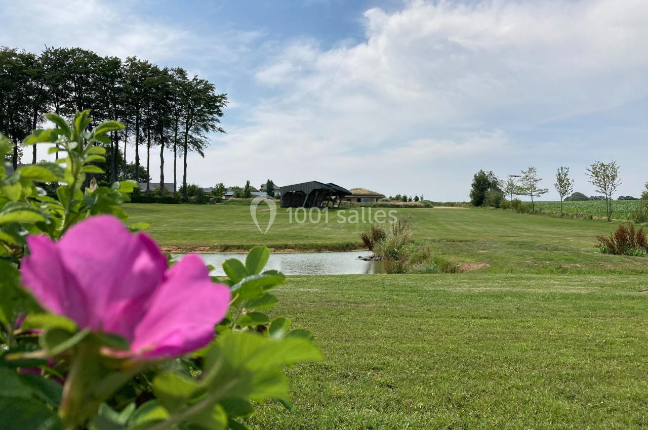 Fleur rose au premier plan avec un étang, une pelouse verdoyante et un bâtiment moderne en arrière-plan.
