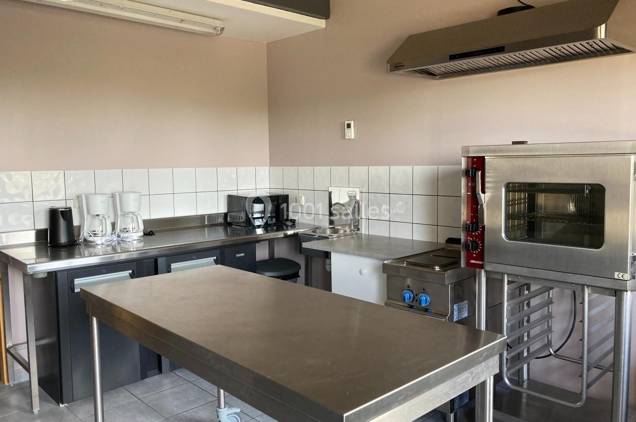 Cuisine professionnelle équipée avec plan de travail en inox, four, cafetières, grille-pain et hotte murale.
