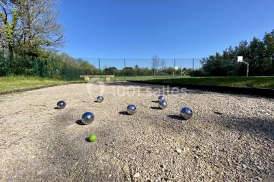 Miniature Boulodrome Grande maison en pierre entourée d'un jardin fleuri et arboré, sous un ciel clair.