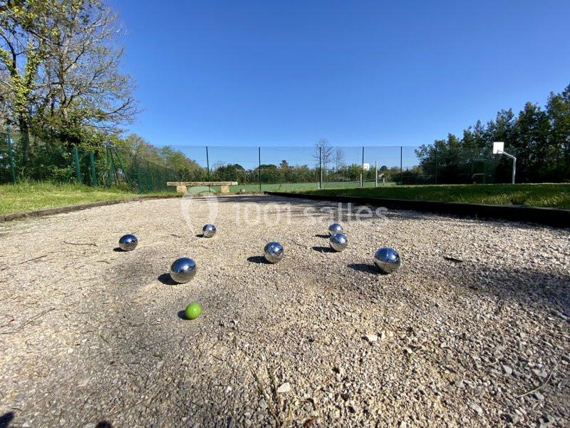 Boulodrome Terrain de pétanque avec plusieurs boules métalliques et un cochonnet vert, entouré de verdure et d'un terrain de sport.