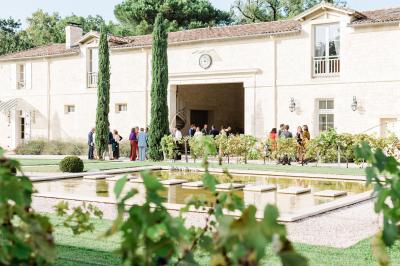 Miniature Extérieur Château Gassies Grande maison en pierre entourée d'un jardin fleuri et arboré, sous un ciel clair.