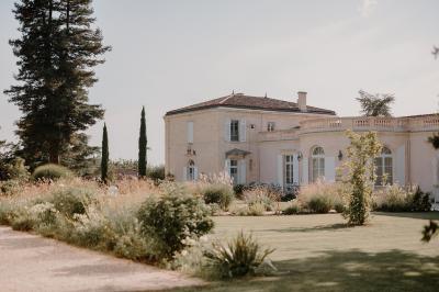 Miniature Extérieur Château Gassies Grande maison en pierre entourée d'un jardin fleuri et arboré, sous un ciel clair.