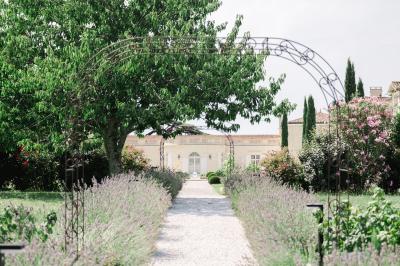 Miniature Extérieur Château Gassies Grande maison en pierre entourée d'un jardin fleuri et arboré, sous un ciel clair.