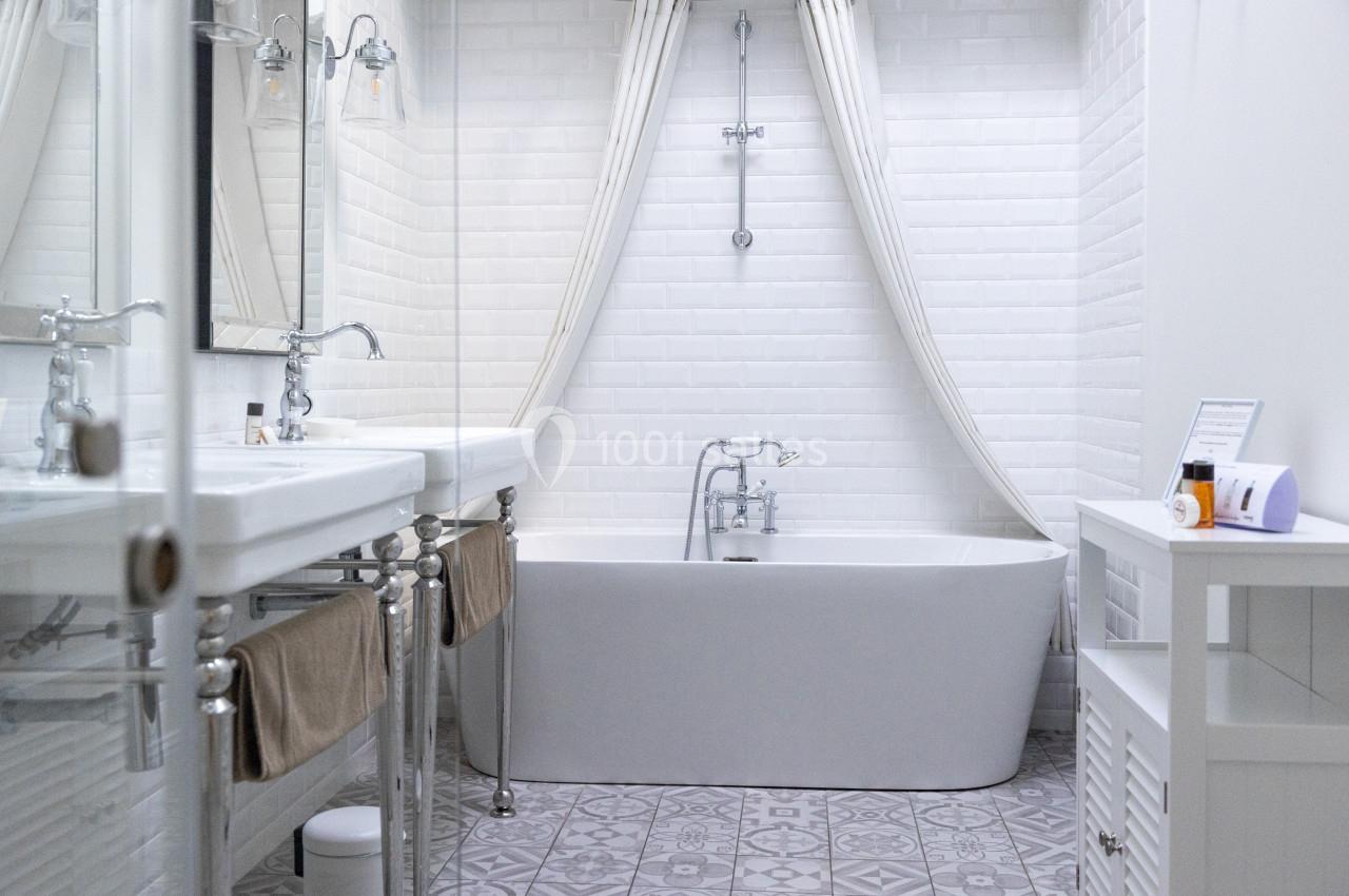 Salle de Bain - Suite Salle de bain lumineuse avec baignoire blanche, rideaux ouverts, carrelage à motifs et double vasque.