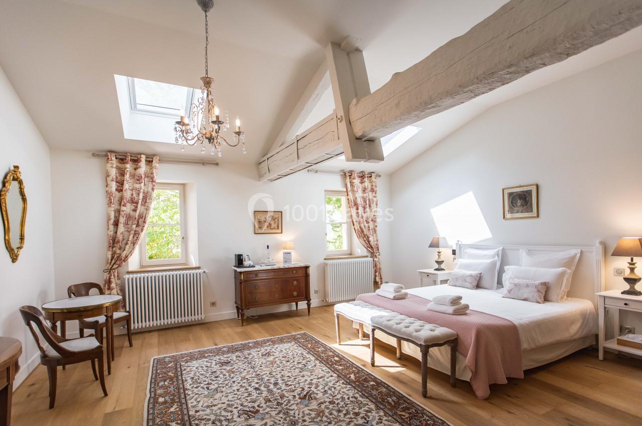 Suite Séquoia Chambre lumineuse avec lit double, poutres apparentes, tapis, mobilier classique et fenêtres laissant entrer la lumière…