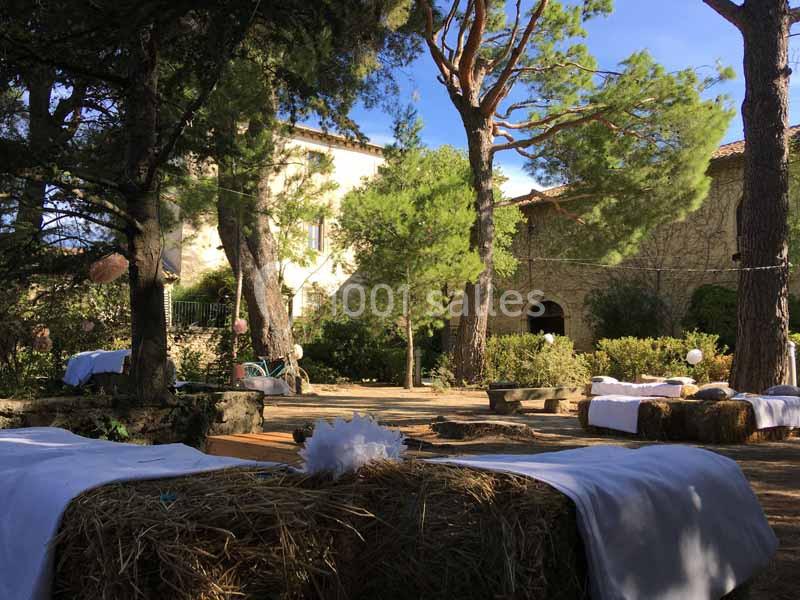 Des ballots de paille recouverts de tissus blancs disposés sous des arbres dans une cour ensoleillée.