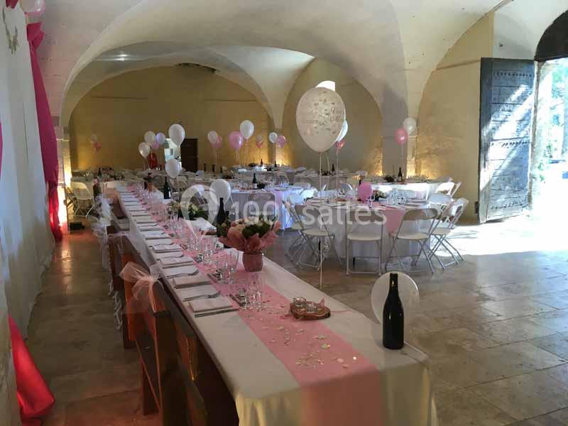 Salle voûtée décorée pour une réception avec tables dressées, nappes blanches, ballons roses et blancs.