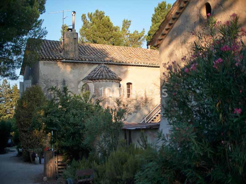 Bâtisse ancienne en pierre avec toit en tuiles, entourée de végétation et éclairée par une lumière douce.