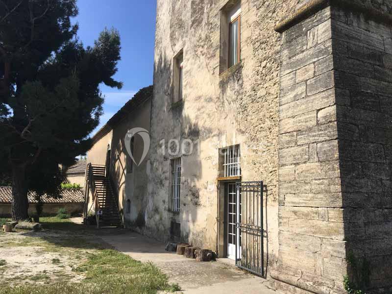 Façade en pierre d'un bâtiment ancien avec une porte grillagée, des fenêtres et un escalier extérieur en bois.