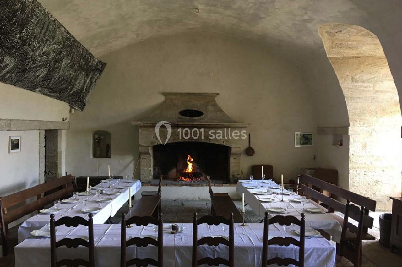 Salle à manger rustique avec tables dressées, cheminée en pierre allumée et murs en pierre apparente.