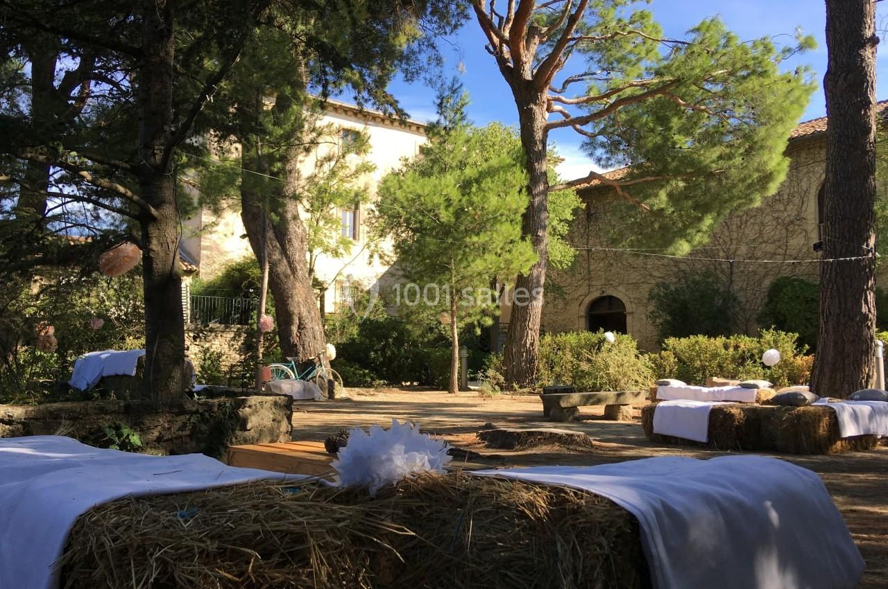 Cour extérieure ombragée avec des bottes de paille recouvertes de tissus blancs, entourée d'arbres et d'un bâtiment en…