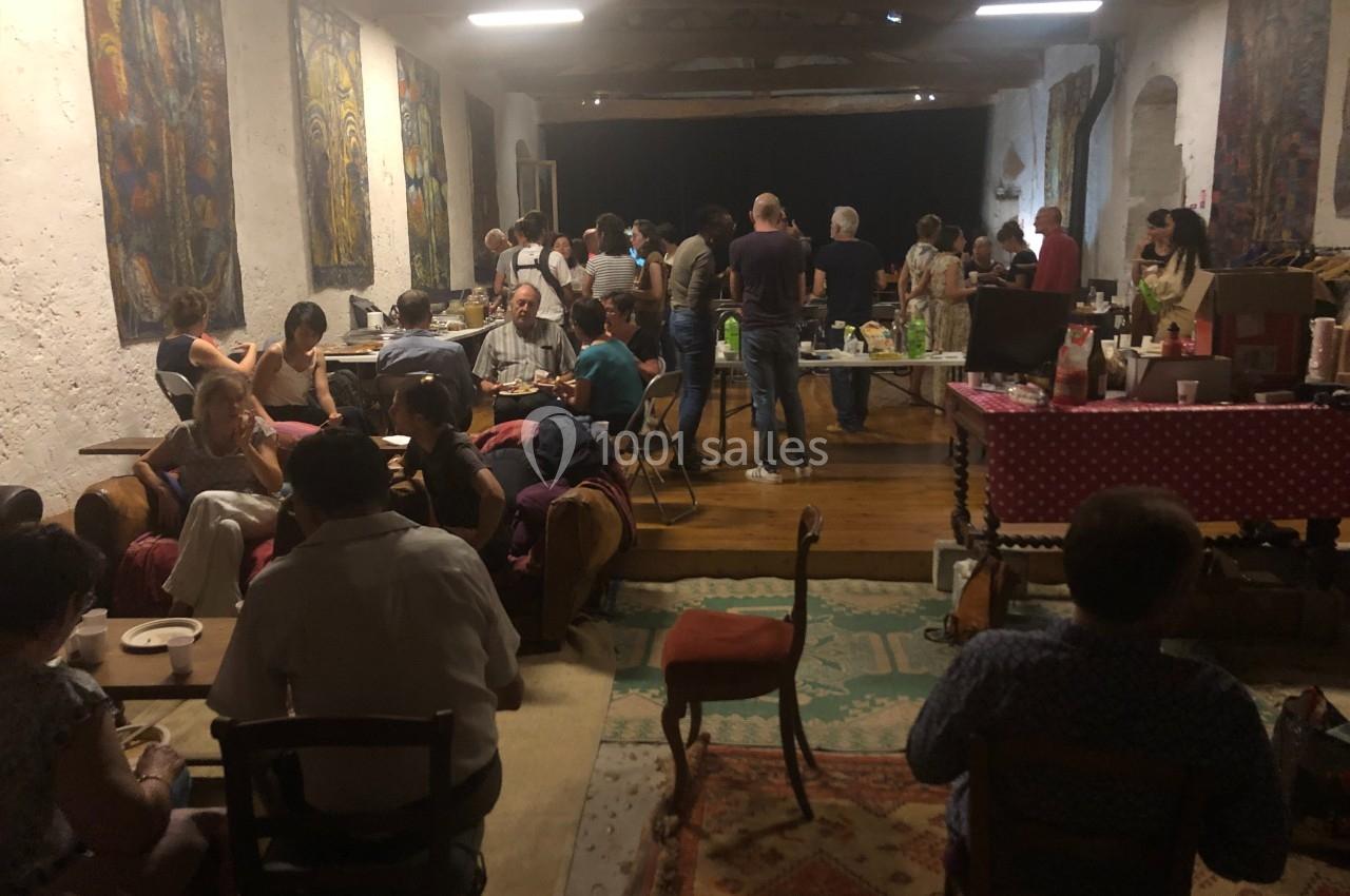 Personnes réunies dans une grande salle rustique, partageant un repas autour de tables et buffets.