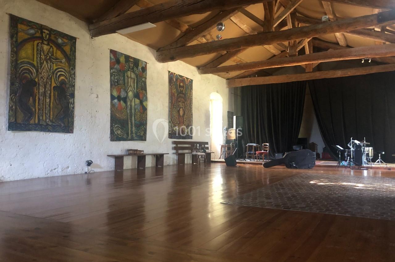Salle spacieuse avec parquet en bois, poutres apparentes, tapis, tableaux colorés et instruments de musique installés.