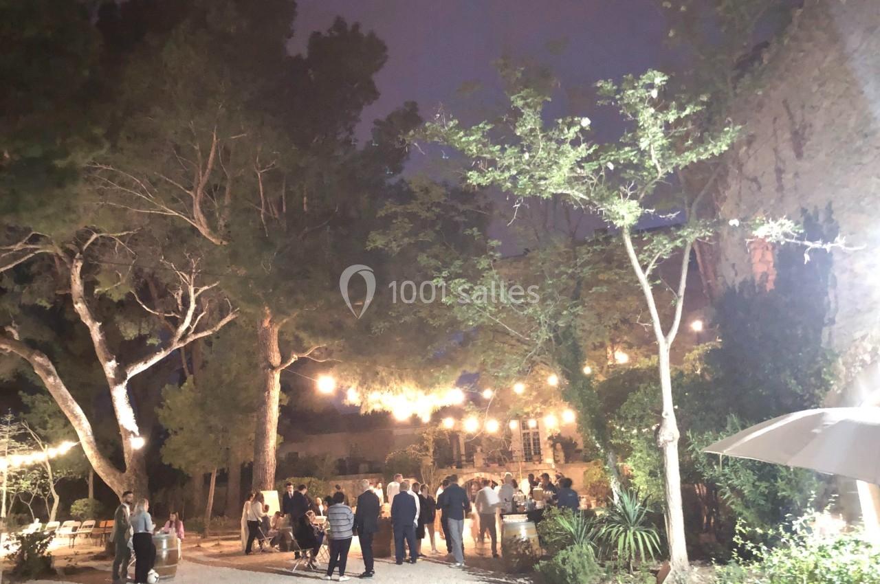 Groupe de personnes rassemblées en soirée dans une cour éclairée par des guirlandes lumineuses, entourée d'arbres.