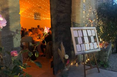 Plan de table sur un chevalet près de l'entrée d'une salle éclairée par des guirlandes lumineuses, ambiance festive.