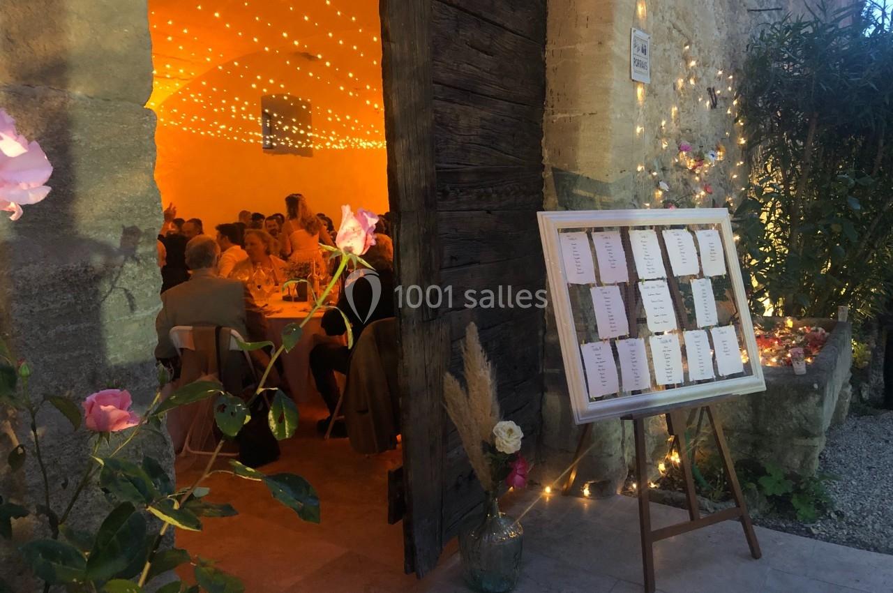 Plan de table sur un chevalet près de l'entrée d'une salle éclairée par des guirlandes lumineuses, ambiance festive.