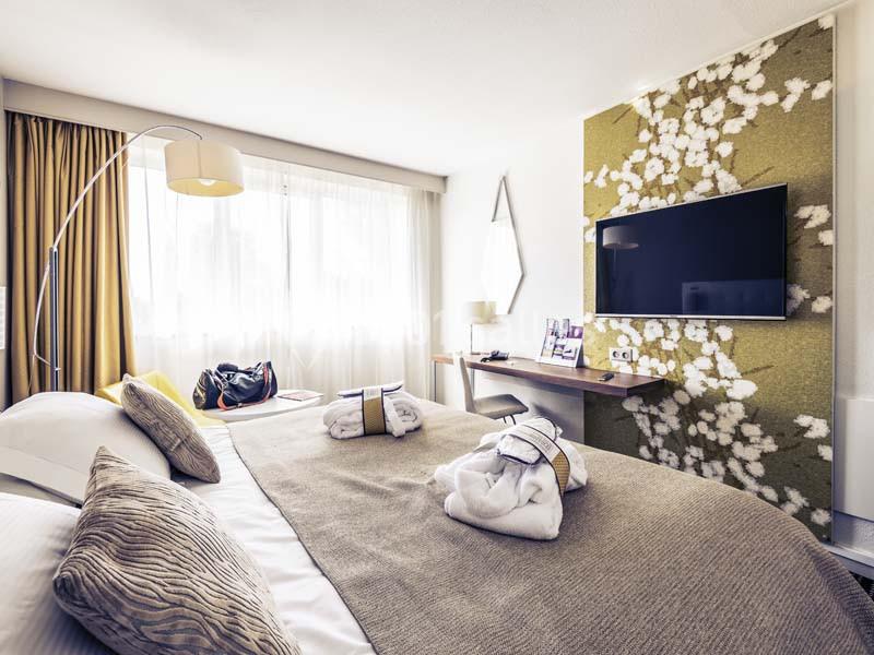 Chambre d'hôtel lumineuse avec un lit double, une télévision murale, un bureau et une décoration florale sur le mur.