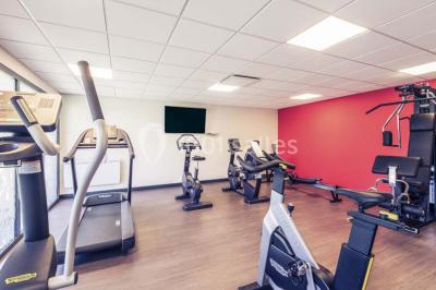 Salle de sport lumineuse avec tapis de course, vélos d'appartement et équipements de musculation.