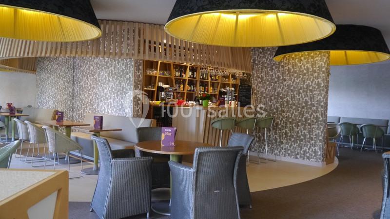 Intérieur d'un café moderne avec tables, chaises en osier, bar en bois et grandes suspensions lumineuses.