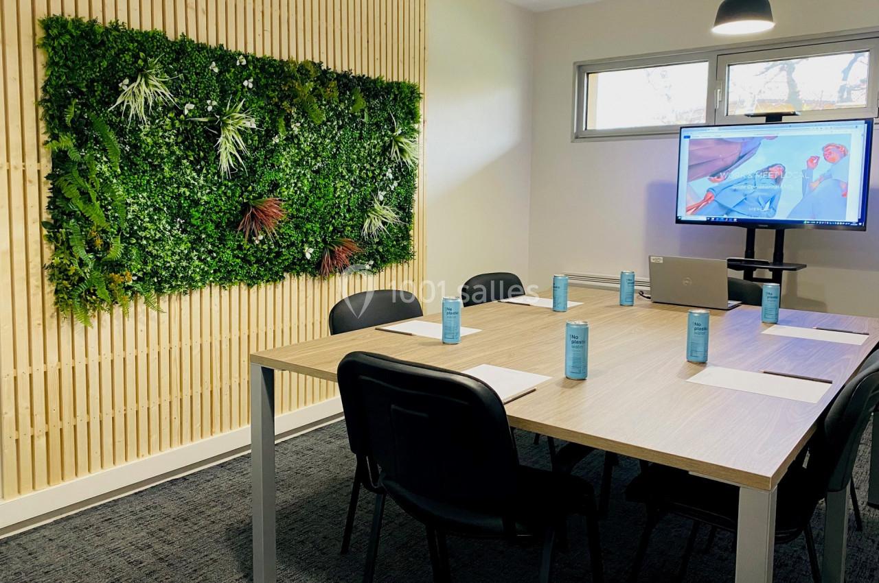 Salle de réunion moderne avec mur végétal, table en bois, chaises noires, écran allumé et lumière naturelle.