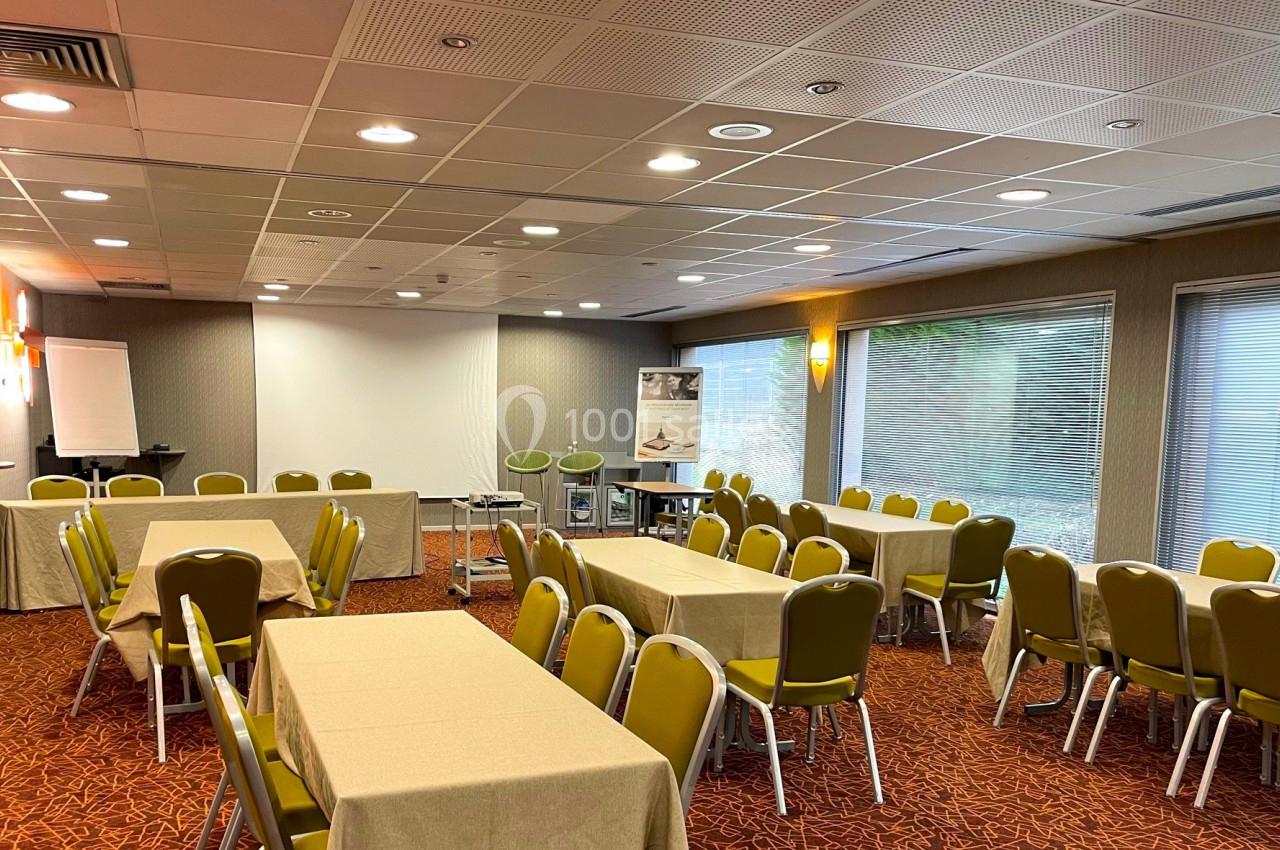 Salle de réunion lumineuse avec tables rectangulaires couvertes de nappes beige, chaises vertes et équipement de…