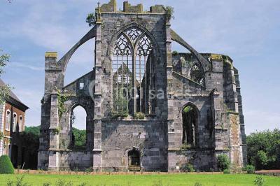Ruines d'une abbaye gothique avec des arches et des fenêtres sans vitraux, entourées de végétation.