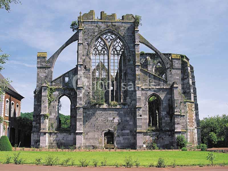 Ruines d'une abbaye gothique avec des arches et des fenêtres sans vitraux, entourées de végétation.