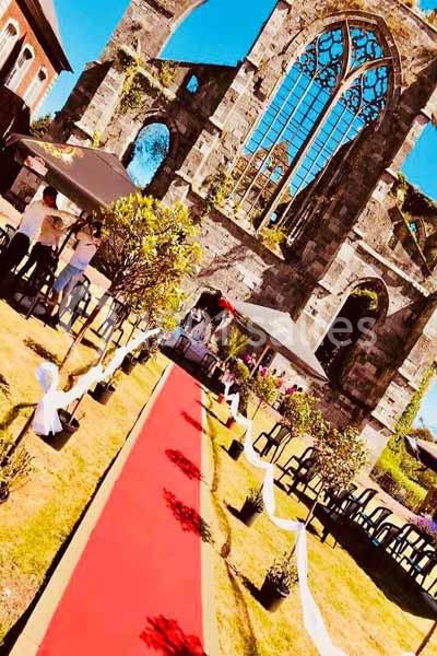 Allée rouge bordée de plantes menant à une cérémonie en plein air devant les ruines d'une ancienne église.
