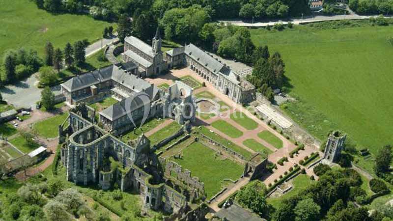 Vue aérienne d'une abbaye historique entourée de jardins aménagés et de verdure, avec des bâtiments en ruines et restaurés.