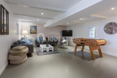 Salle de séjour lumineuse avec canapé, baby-foot, table basse en bois, télévision et décoration moderne.