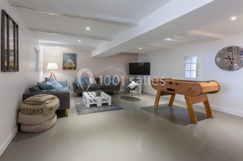 Salle de séjour lumineuse avec canapé, baby-foot, table basse en bois, télévision et décoration moderne.