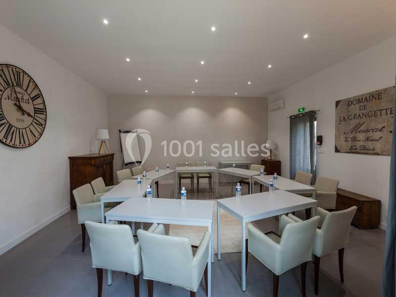 Salle de réunion lumineuse avec tables disposées en U, chaises rembourrées, tableau de conférence et décorations murales.