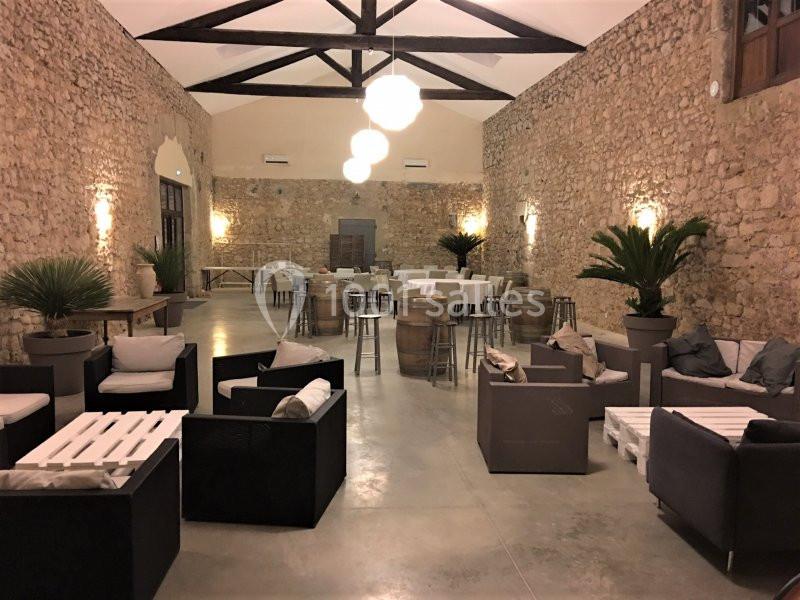 Salle spacieuse avec murs en pierre, mobilier moderne, tables hautes et plantes décoratives.