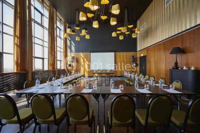 Chambre moderne avec lit double, bureau équipé, grande fenêtre avec vue sur les toits et éclairage suspendu.