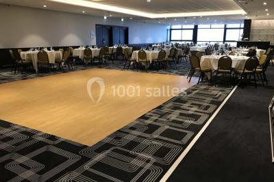 Chambre moderne avec lit double, bureau équipé, grande fenêtre avec vue sur les toits et éclairage suspendu.