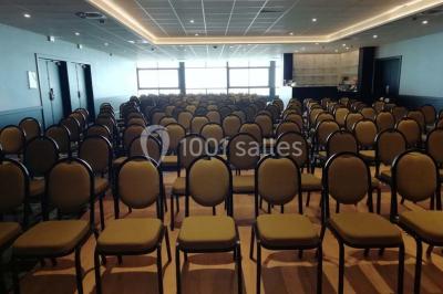 Chambre moderne avec lit double, bureau équipé, grande fenêtre avec vue sur les toits et éclairage suspendu.