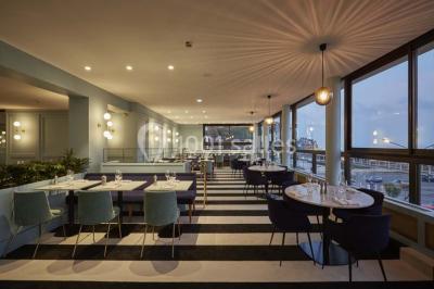 Chambre moderne avec lit double, bureau équipé, grande fenêtre avec vue sur les toits et éclairage suspendu.