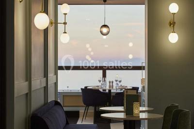 Chambre moderne avec lit double, bureau équipé, grande fenêtre avec vue sur les toits et éclairage suspendu.