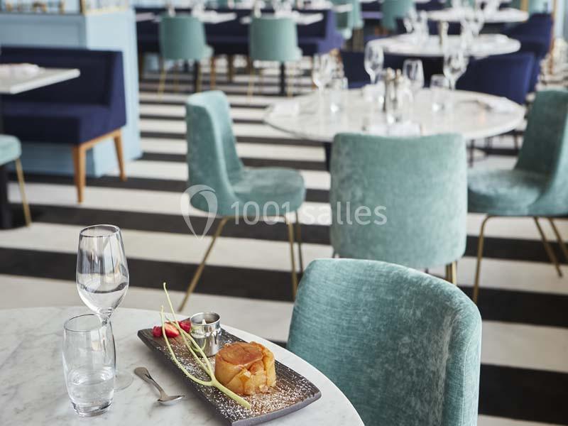Une table de restaurant élégante avec un dessert dressé, entourée de chaises en velours et d'un sol rayé noir et blanc.
