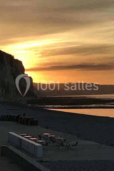 Coucher de soleil illuminant des falaises et une plage de galets avec quelques tables en premier plan.