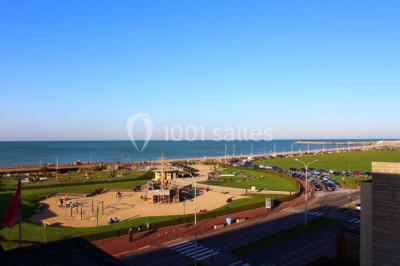 Chambre moderne avec lit double, bureau équipé, grande fenêtre avec vue sur les toits et éclairage suspendu.